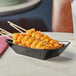 A black Tablecraft serving basket with food on sticks.