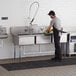 A man cleaning a Regency stainless steel three compartment sink.