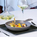 A stone gray RAK Porcelain Chef's Fusion frying pan with food on a plate on a table in a fine dining restaurant.