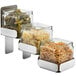 A group of Rosseto square glass condiment jars filled with food on a counter.