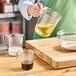 A person holding a Choice clear plastic measuring cup with yellow liquid.