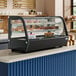 An Avantco black refrigerated countertop bakery display case with food on it.