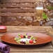 A RAK Porcelain flat coupe plate with food, fruit, and flowers on a table.