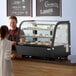 A man and woman standing at a counter with food in an Avantco refrigerated countertop bakery display case.