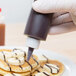 A person using a Tablecraft squeeze bottle to pour syrup over a plate of pancakes.