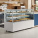 An Avantco white curved glass dry bakery display case on a counter with trays of pastries.