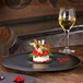 A RAK Porcelain Volcano Black plate with a dessert and wine on a table.