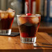 A glass of Monin root beer flavored liquid with ice cubes and a cherry on top.
