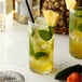 Two glasses of pineapple and lime drinks with straws, pineapple slices, and mint leaves.