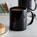 A black Acopa stoneware mug filled with coffee on a counter.