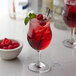 A glass of red liquid with a straw and a bowl of raspberries on a table in a cocktail bar.