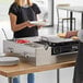 A woman using a Choice Deluxe Butane Pancake Station to make a pancake on a table outdoors.