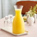 A Libbey plastic carafe filled with yellow liquid on a tray with glasses.