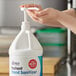 A person using a white plastic pump to dispense hand sanitizer from a white jug.