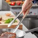A person using Vollrath stainless steel tongs with tan Kool-Touch handles to cook steak.