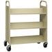 A tan metal Hirsh Industries book cart with black wheels.