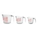 A group of three Anchor Hocking clear glass measuring cups with red writing and handles.