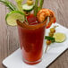 A glass of Clamato tomato cocktail with shrimp and vegetables on top.