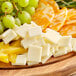 A wooden cutting board with a solid block of Savoldi whole milk mozzarella cheese, grapes, and green fruit.