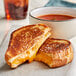 A grilled cheese sandwich cut in half on a plate with tomato soup.