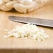 A knife next to a pile of peeled garlic on a cutting board.