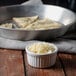 A white bowl and a pan of shredded Asiago cheese.