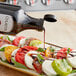 A bottle of Colavita Balsamic Glaze being poured over a plate of tomatoes, cheese, and basil.