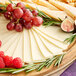 A plate with a block of Walnut Creek Foods Monterey Jack Cheese, grapes, and figs.