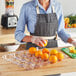 A woman in a kitchen using a Marco Company clear plastic tray to prepare oranges.