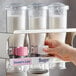 A hand using a Server InSweeten coffee sweetener dispenser to pour white powder.