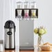 A Server InSweeten triple coffee sweetener dispenser station on a hotel buffet table with a coffee machine and a container of sugar.