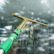 An Unger GoldenClip window squeegee with a brass handle cleaning a window.