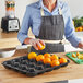 A woman in a kitchen using a black Marco Company produce riser to hold oranges.