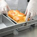 A hand in a glove holding a loaf of bread in a Chicago Metallic aluminized steel bread loaf pan.