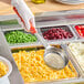 A person using a Vollrath Orange Perforated Round Spoodle to put food in a tray.