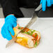 A person in blue gloves using a Dexter-Russell V-Lo Scalloped Offset Bread and Sandwich Knife to cut a sandwich.