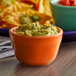 A Tuxton papaya china bowl filled with guacamole and tortilla chips on a table.