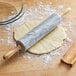 A white marble rolling pin with wood handles and base rolling out dough.