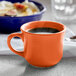 A Tuxton round papaya china cup filled with coffee on a counter.