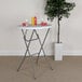 A Flash Furniture round white plastic folding table with a plant on it in front of a tree.