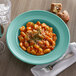 A bowl of pasta with a fork on a table with a glass of wine.