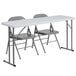 A white rectangular folding table with a white surface and two grey chairs.