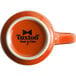 An orange Tuxton mug with a white rim and black text on the front.