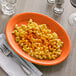 A Tuxton papaya oval china platter with a plate of macaroni and cheese and a fork.