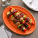 A Tuxton oval china platter with skewers and vegetables on it.