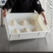 A person holding a white Baker's Mark dough proofing box on a white surface with dough inside.