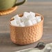 An American Metalcraft copper oval bowl filled with sugar cubes on a table.