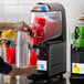 A person pouring red liquid into a Vollrath juice machine.