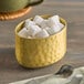 An American Metalcraft gold aluminum sugar packet holder filled with sugar cubes on a table.