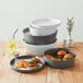 A stack of gray plastic serving bowls with burgers and fries on a table.